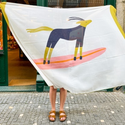 Lenço branco com estampa de animal colorido segurado por pessoa com sandálias na calçada