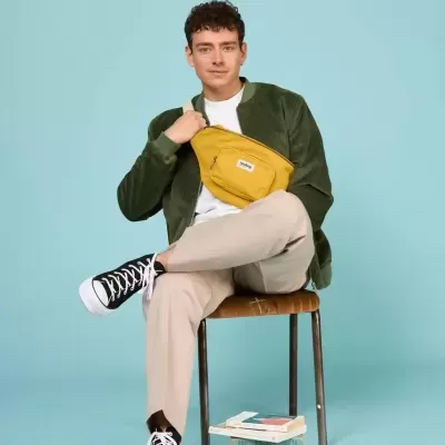 Homem sentado com mala tiracolo amarela e roupa casual