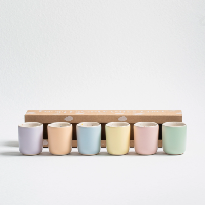 Seis pequenos vasos de cerâmica em cores pastel alinhados diante de uma caixa castanha com padrões brancos