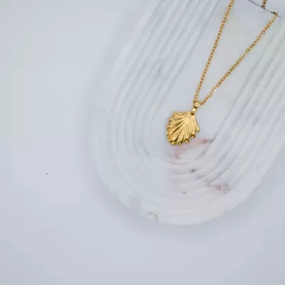 Colar dourado com pendente de concha sobre base branca texturizada
