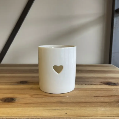 Copo branco de cerâmica com recorte de coração sobre mesa de madeira