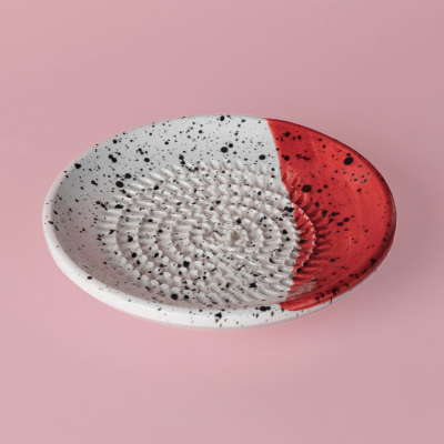 Prato cerâmico branco e vermelho com manchas pretas e textura espiral sobre fundo rosa