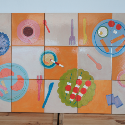 Painel de azulejos pintados com motivos de comida e utensílios de cozinha, em tons de laranja, azul, verde e vermelho.