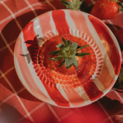 Prato de cerâmica listrado com morango em fundo de pano xadrez vermelho com morangos.