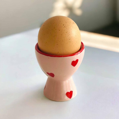 Suporte para ovo rosa claro com corações vermelhos e um ovo castanho