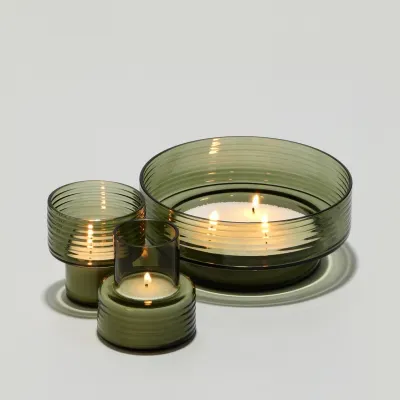 Três velas em recipientes de vidro verde translúcido com textura às riscas horizontais.