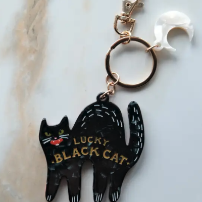 Chaveiro de gato preto com texto amarelo e argola metálica dourada