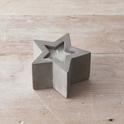 Vela branca em suporte de concreto cinza formato estrela sobre superfície de madeira clara