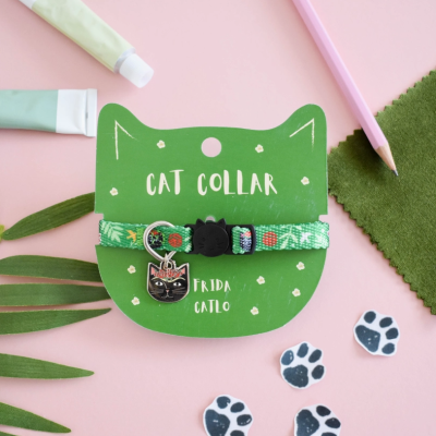 Colar para gato verde com medalha preta em embalagem de cartão verde em forma de rosto de gato sobre fundo rosa