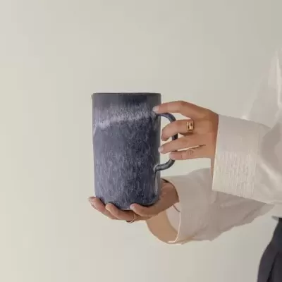 Caneca azul escuro marmoreada a ser segurada por mão com anéis em fundo neutro