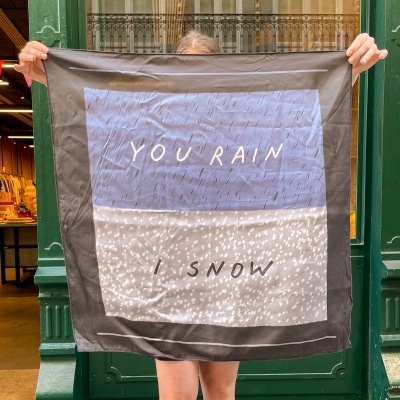 Lenço quadrado com texto YOU RAIN e I SNOW em fundo azul e branco, segurado por pessoa em frente a porta verde