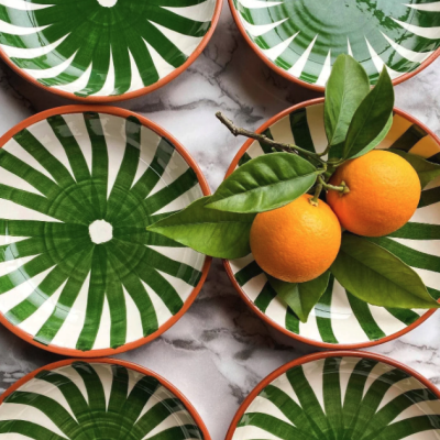 Pratos decorativos verdes e brancos com bordas laranja e dois frutos laranja sobre um prato