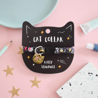 Coleira para gato com padrão espacial e pendente dourado num cartão preto em formato de cabeça de gato