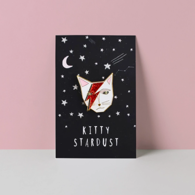 Pin rosto de gato vermelho e dourado em cartão preto com estrelas e texto Kitty Stardust