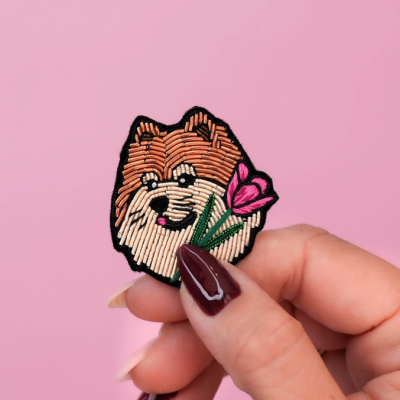 Patch bordado rosto de cão com flor rosa segurado por mão com unhas vermelhas