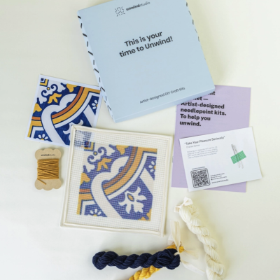 Kit de ponto cruz com padrão colorido e linhas para bordar, embalagem azul da Unwind Studio.