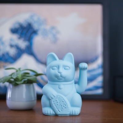 Figura decorativa de gato da sorte azul claro com planta e pintura ao fundo