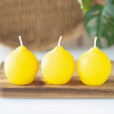 Três velas amarelas em forma de limão sobre tábua de madeira
