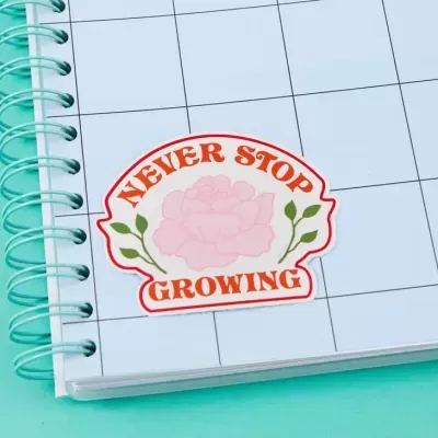 Adesivo 'NEVER STOP GROWING' com flor rosa em caderno azul