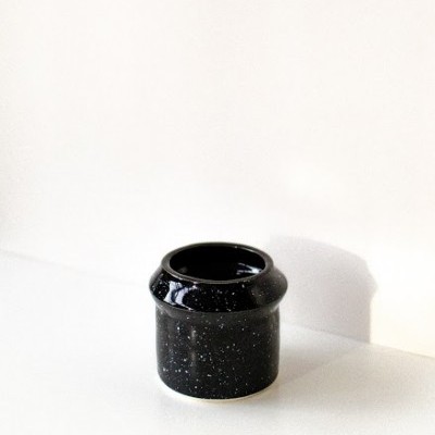 Frasco preto cilíndrico com pontos em fundo branco