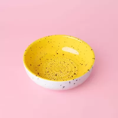 Tigela redonda amarela com exterior branco e manchas pretas, sobre superfície rosa