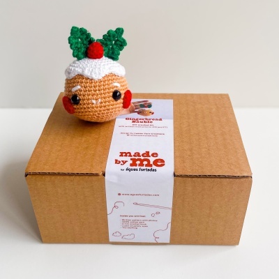 Caixa de embalagem castanha com rótulo branco e figura de crochê de pudim de Natal