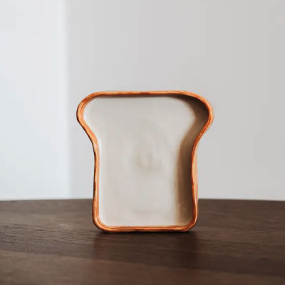 Prato cerâmico em forma de fatia de pão com bordas castanhas e interior creme