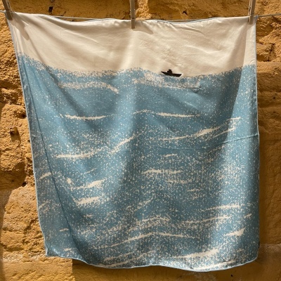 Toalha ou tecido azul e branco com padrão de ondas do mar e barco preto.