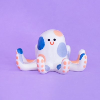 Figura decorativa polvo em cerâmica com manchas coloridas e sorriso em fundo roxo