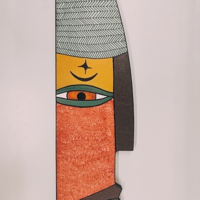 Escultura decorativa vertical colorida com padrão geométrico formando uma face estilizada.