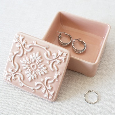 Caixa decorativa rosa em cerâmica com argolas e anel prateado sobre tecido claro