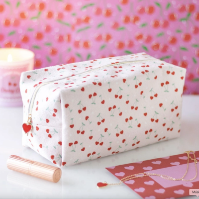 Necessaire branca com padrão de cerejas vermelhas e verdes, zíper com puxador vermelho em forma de coração.
