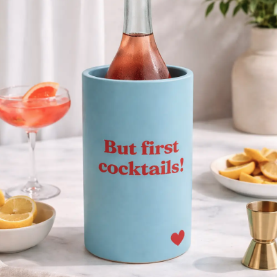 Suporte azul com texto vermelho para garrafa numa mesa com cocktail, limões e doseador.