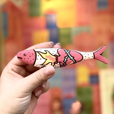 Boneco peixe colorido com decoração com pintas pretas em fundo desfocado colorido.