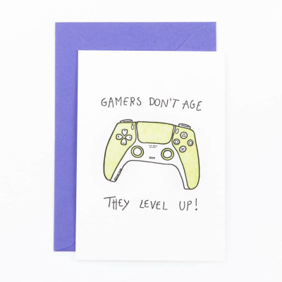 Cartão com comando de videojogo verde e texto GAMERS DONT AGE THEY LEVEL UP! com envelope roxo