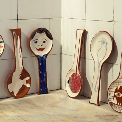 Seis colheres de cerâmica decorativa com vários padrões e cores numa parede de azulejos brancos