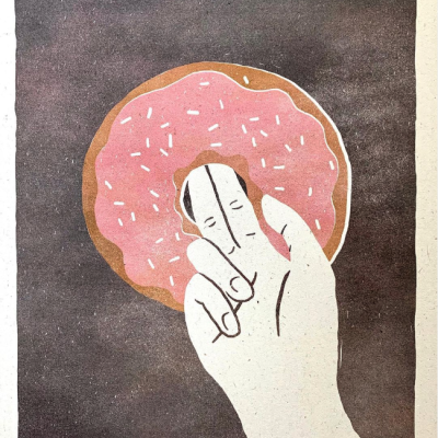 Mão branca segurando uma rosquinha rosa com granulados num fundo castanho.