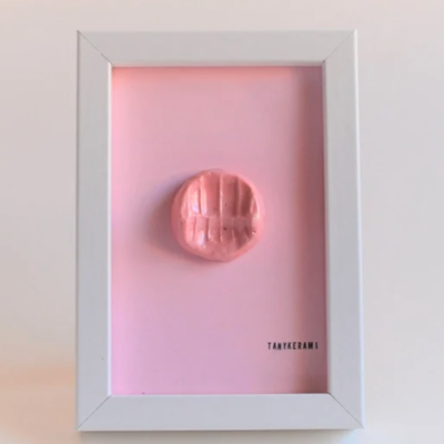 Moldura branca com fundo rosa e objeto cerâmico vermelho no centro