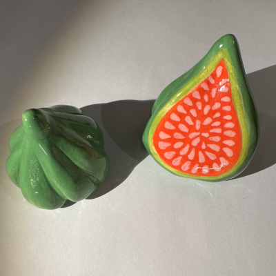 Objetos de cerâmica em forma de frutas, um verde e outro em forma de figo laranja e verde