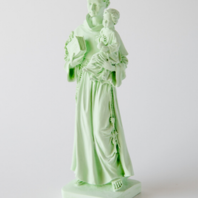 Estátua de santo verde claro segurando criança e livro em fundo branco