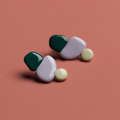 Brincos geométricos com cores verde, lilás e amarelo claro sobre fundo rosa