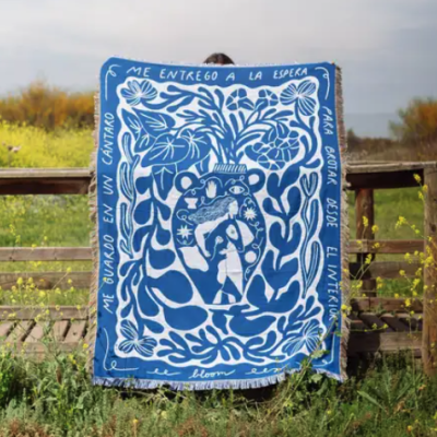 Manta azul e branca com padrão artístico e texto em espanhol pendurada em cerca de madeira ao ar livre