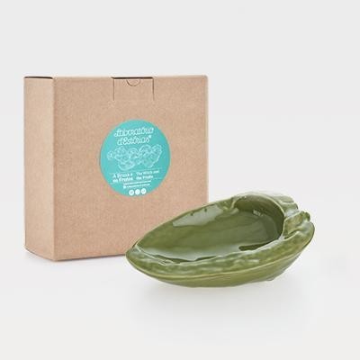 Prato cerâmico verde em forma de folha ao lado de caixa de embalagem de cartão com etiqueta azul