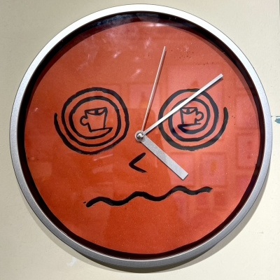 Relógio de parede redondo vermelho com desenho de rosto e xícaras de café nos olhos