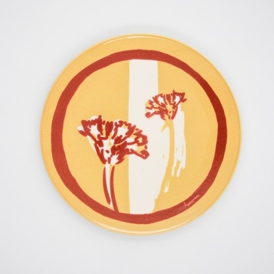 Prato redondo amarelo com borda vermelha e flores vermelhas e brancas no centro.