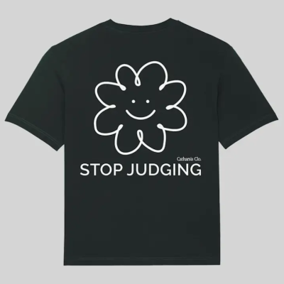 T-shirt preta com desenho de flor sorridente branca e texto 'STOP JUDGING' na parte de trás