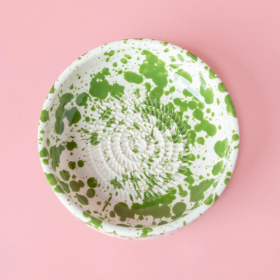 Prato redondo com manchas verdes sobre fundo branco numa superfície rosa