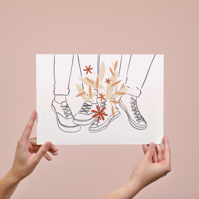 Desenho de três pares de ténis com flores e folhas coloridas, mãos a segurar o papel