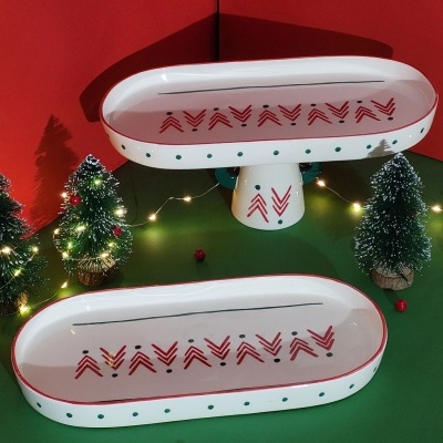 Dois tabuleiros cerâmicos brancos com padrão geométrico vermelho e pontos verdes, decorados com mini árvores de Natal e luzes