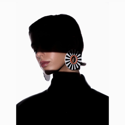 Brincos redondos preto, branco e laranja em rosto de pessoa com roupa preta